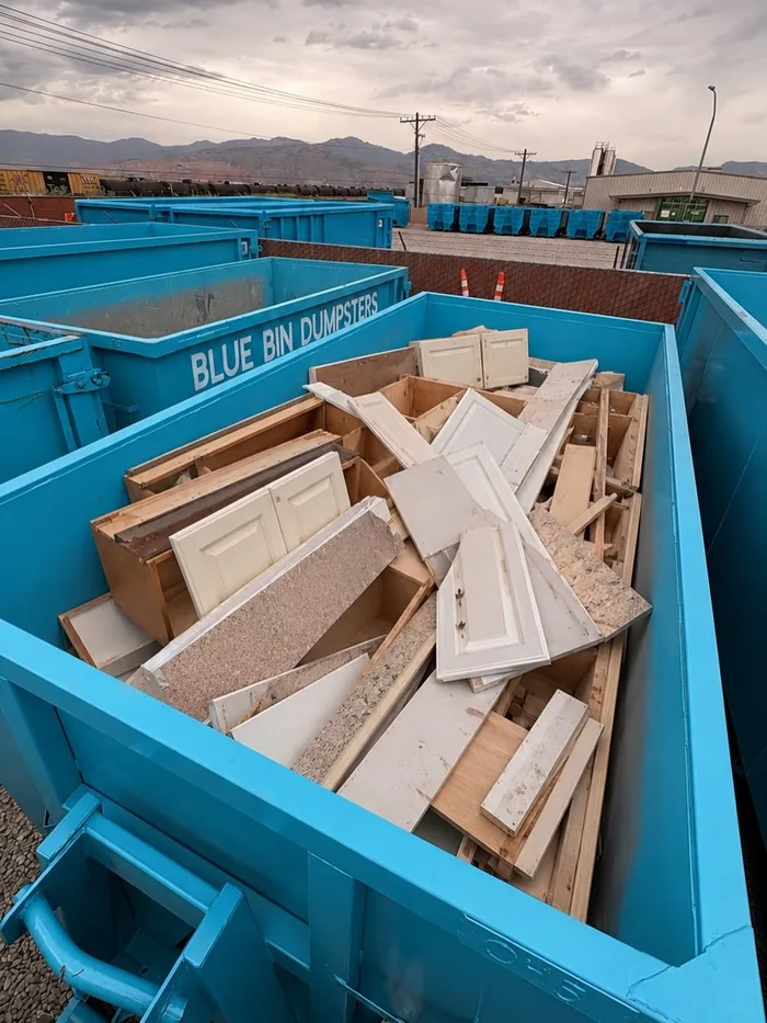 A Blue Bin dumpster filled with old kitchen cabinets and countertops